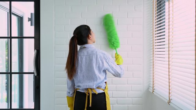 4k video of Housekeeper Young female spring cleaning house interior holding a duster for wiping dust dusting furniture at home