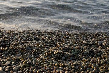 pebble stones by the sea. Silky waves of blue sea from long exposure.