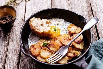 Fried Eggs and Potatoes in cast iron skillet on rustic wooden table. Skillet Breakfast. Selective focus