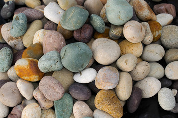 Multi-coloured beach pebbles piled. Green, Purple and white pebbles, Small rocks