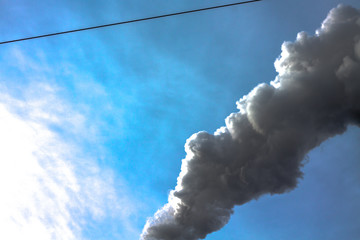 Closeup of dirty dark smoke clouds from a high industrial chimney against a clean blue sky