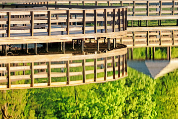Obraz premium wooden trail bridge over water in park abstract landscape background. Walking pathway reflection in calm water. City outdoor activity area