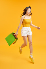 Beautiful shopaholic young woman jumping in the air with shopping bags over orange background.