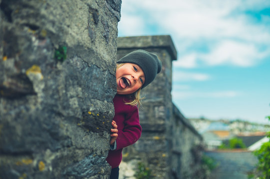 Smiling preschooler peeping from behind wall in small town