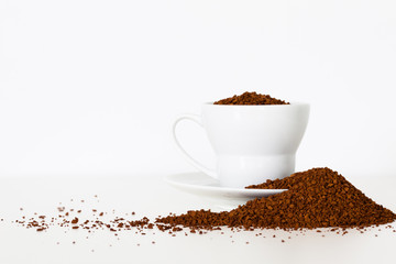 Closeup of coffee cup beautifully displayed with a pile of instant coffee grains isolated on white background. Copy space.