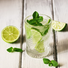 Refreshing cold drink with lime and mint in a glass on a white wooden board table. Traditional summer mojito cocktail. Selective focus, copy space