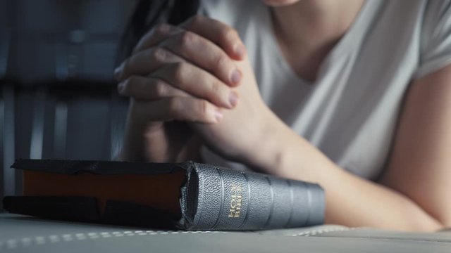 girl praying indoors at bedtime on bible. religion concept evening prayer woman brunette hands on bible praying by lifestyle bed