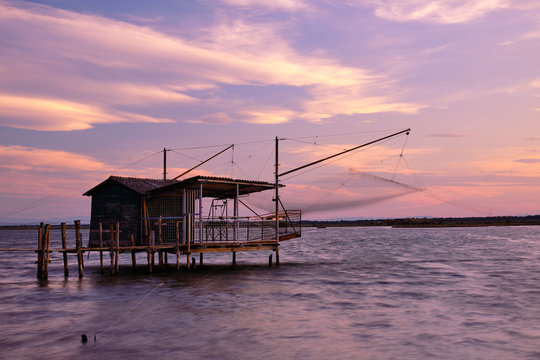 Amazing fishing hut in sunset with slk effect sea in Piallassa della Baiona, Ravenna, Italy.
Sky with yellow clouds and windy time