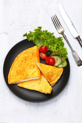 Omelette with cheese and fresh vegetables on a black porcelain plate. Concept of healthy and delicious breakfasts. Copy of the space.Top view.