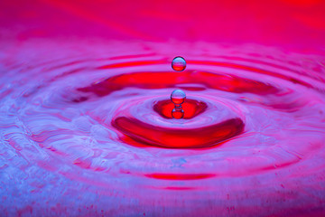 splash of a drop of water on a color gradient burgundy violet surface close-up