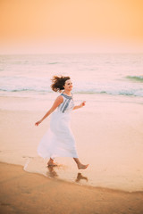 Goa, India. Young Caucasian Woman With Fluttering Hair In Wind In White Dress Walking Along Seashore, Enjoying Life And Smiling In Summer Sunlight
