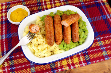 Sausage and mashed potato meal with mushy peas in a metal enamel dish
