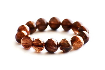 Mica rutilated quartz bracelet on white background.  Brown crystal bracelet gemstones.  Selective focus on the front part of the bracelet and leave the blurry part and the empty part to be copy space.
