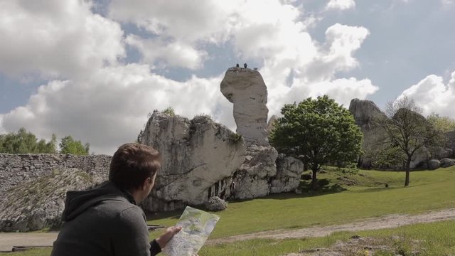 Man Sitting And Holding A Map Looking At The Beautiful Landscape Of Camel's Rock Formation Next To The Ruins Of Ogrodzieniec Castle In Poland. - wide shot