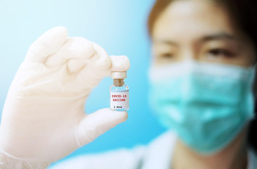 A female Asian physician with surgical mask and white rubber gloves at a clinic, holding a glass bottle of 1 dose covid-19 vaccine, with white background and red letters.