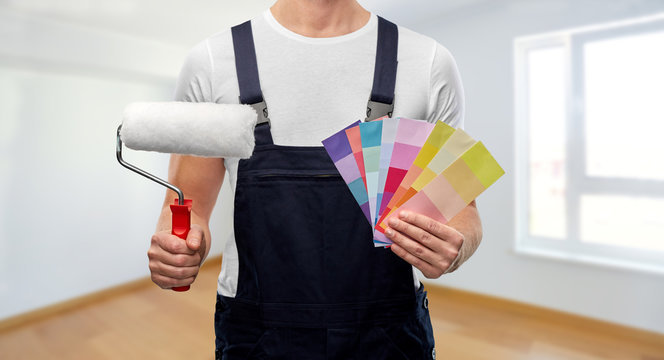 repair, construction and building - close up of painter or builder with paint roller and color charts over empty room of new home on background
