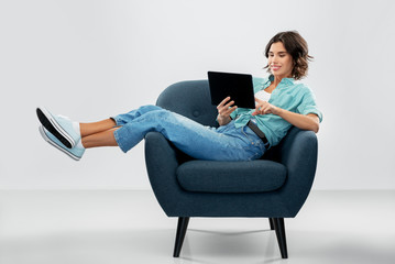 people and technology concept - portrait of happy smiling young woman with tablet pc computer sitting in modern armchair over grey background - Powered by Adobe