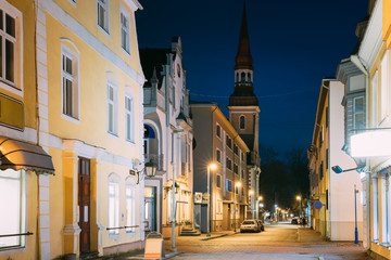 Fototapeta premium Parnu, Estonia. Night Nikolai Street With Old Houses, Restaurants, Cafe, Hotels And Shops In Evening Night Illuminations. View Of Lutheran Church Of St. Elizabeth On Background