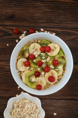 A rich and healthy breakfast. Oatmeal porridge with fruit and berries with kiwi banana and cherry. Diet concept. Natural and eco friendly food on a wooden table with copy space for text