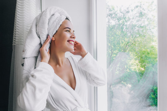 Young Beautiful Woman In White Towel And Robe Locking Through The Window At Home