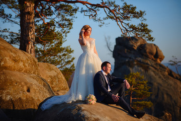 The bride and groom are standing on top of a cliff. Sunset.