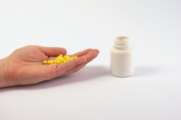 Obraz premium Hand with pills, pills, vitamins and an adjacent white jar. The purpose of treatment, medications, vitamins. Taking painkillers. Copy space