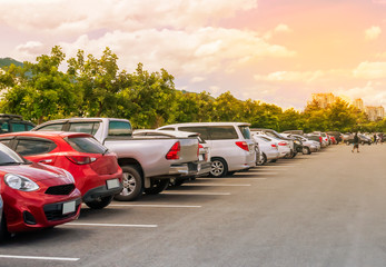 Car parking in large asphalt parking lot with trees, white cloud and blue sky background. © merrymuuu