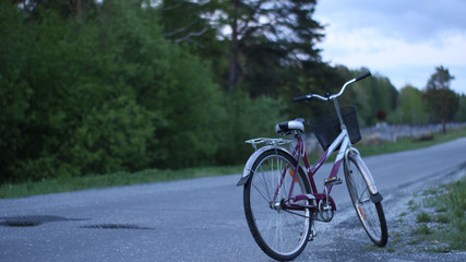 Fototapeta na wymiar a lonely bicycle on a deserted road at the edge of the woods outside the city at evening dusk
