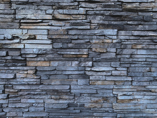 Unshaped gray stone wall pattern. made of the multi colour rocks. Stone cladding wall made of striped stacked slabs of natural brown rocks.