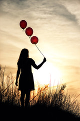 Girl holds balloons in hand sunset during sunset