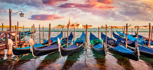 Fototapeta na wymiar Panoramic summer view of the gondolas parked beside the Riva degli Schiavoni in Venice, Italy, Europe. Captivating mediterranean landscape wit Church of San Giorgio Maggiore on background.