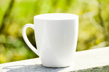 White coffee mug mock up outdoor with blurred background. Tea mug mockup for branding, template, logo, nature blurred background at summer terrace. White cup mock up, cappuccino mug mock-up outdoor.