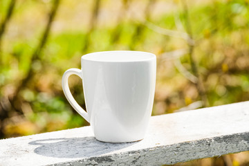 White coffee mug mock up outdoor with blurred background. Tea mug mockup for branding, template, logo, nature blurred background at summer terrace. White cup mock up, cappuccino mug mock-up outdoor.
