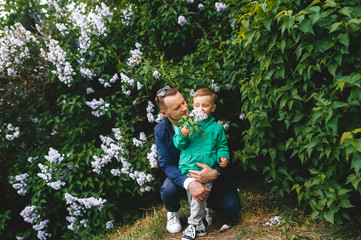 Naklejka na ściany i meble Little boy enjoys smell of blooming lilac. Dad hugs little son