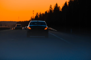 Sunset highway with cars on the country road. Evening orange sunset highway with multiple cars close up. Car trip with scenic road view, evening sun orange sunlight.