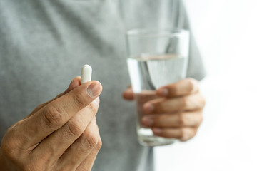 man's hand holding pill or medicine and picking up a glass of water. Men taking medication, feeling ill Health care uses medicine concepts.