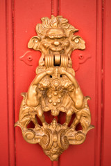 Vertical picture with old style decorated door knob in shape of satire head and two cupidons on red wooden door in Luberon, heart of Provence, France. Medieval ornamental iron antique decoration.