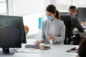 Businesswoman disinfecting her laptop keyboard in the office.	