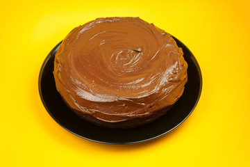 Chocolate cake, homemade pie on yellow background. Whole home cake with cocoa ingredient on black plate