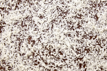 Chocolate cake decorated with flaked coconut, closeup. Homemade pie surface with coconut flakes, background, top view