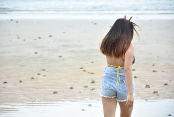 Beach time recreation concept. Young asian model in bikini strolling alone on sea beach. Woman in beachwear swimsuit stroll with on a sea coast.