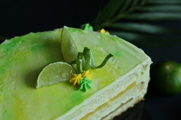 Tropical lime biscuit cake with cream cheese, mango jelly and sweet cream decoration with the lime pieces on top, on the dark background.