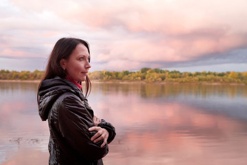 Young woman with dark hair in a black leather jacket on the river Bank at sunset in the autumn, spring or summer evening