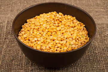 Yellow split peas in a ceramic bowl on a background of coarse-textured burlap. Traditional cereals for making soups and porridge. Close up.