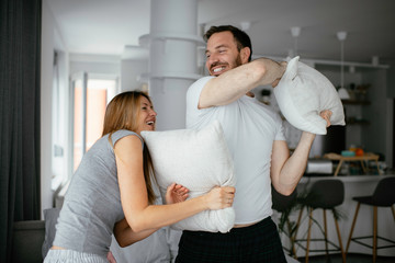 Young couple fighting pillows on the bed. Happy couple having fun at home.	