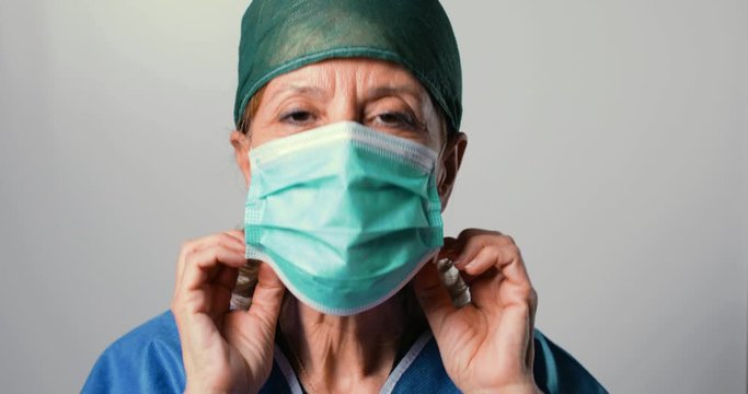 Medico donna si mette correttamente la mascherina chirurgica prima dell'operazione, sfondo bianco.