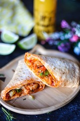 pita sandwich with chicken and vegetables on dark background, lime, orange juice and flowers on the background