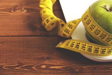 Floor scales, tape measure and green apple on a wood background top view. The concept of a healthy diet, body weight control, down weight. Healthy lifestyle. Copy space