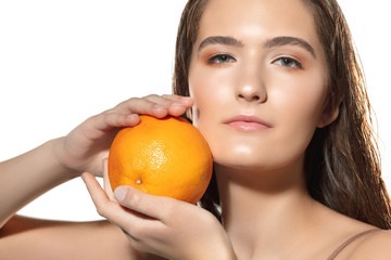 Touch. Close up of beautiful young woman with orange on white background. Concept of cosmetics, makeup, natural and eco treatment, skin care. Shiny and healthy skin, fashion, healthcare.