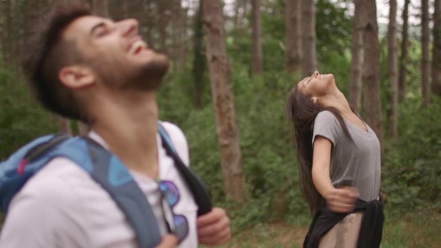 Smiling young couple walking with backpacks at the forest trail